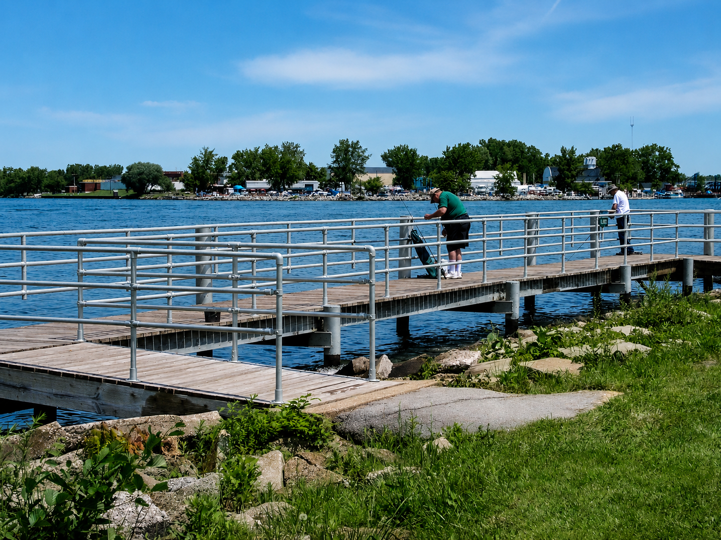 Zwei Männer angeln an einem sonnigen Tag von einem hölzernen Pier mit Metallgeländern, der in einen breiten blauen See ragt. Im Hintergrund sind Bäume, Gebäude und Boote am gegenüberliegenden Ufer zu sehen.